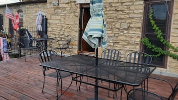 Una terrazza esterna con tavolo e sedie in metallo, un ombrellone a righe e un edificio in pietra sullo sfondo.