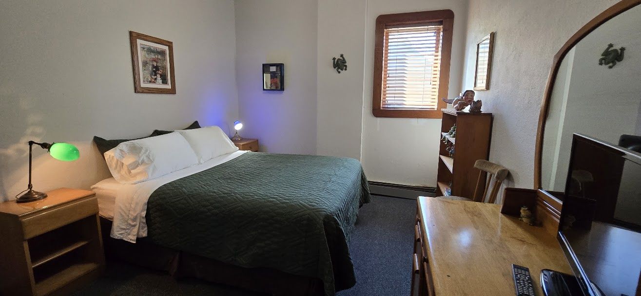 Quarto com cama, mesa de cabeceira, abajur, cômoda e televisão.