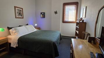 Quarto com cama, mesa de cabeceira, abajur, cômoda e televisão.