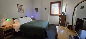 A bedroom with a bed, bedside table, lamp, dresser, and a television.