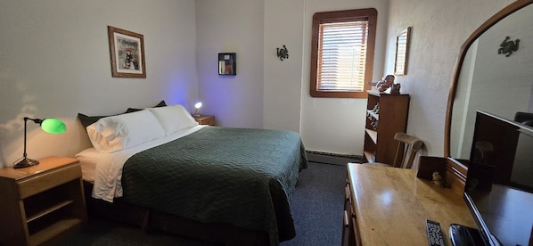 A bedroom with a bed, bedside table, lamp, dresser, and a television.
