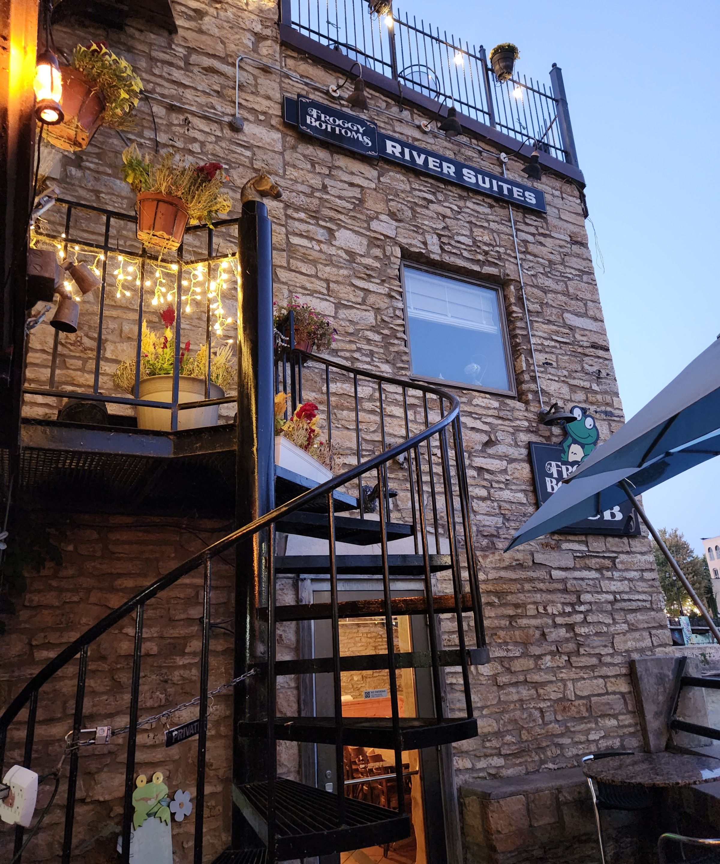 Un immeuble avec une façade en pierre, une enseigne indiquant « River Suites », et un escalier doté d’une rampe en métal.