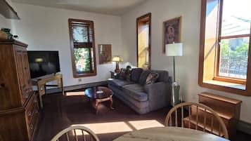 A living room with a sofa, a television, a wooden cabinet, and a dining table.