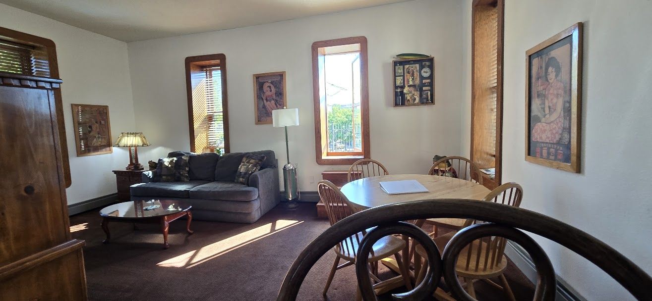 A living room with a sofa, coffee table, dining table, chairs, and artwork on the walls.