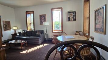 A living room with a sofa, coffee table, dining table, chairs, and artwork on the walls.