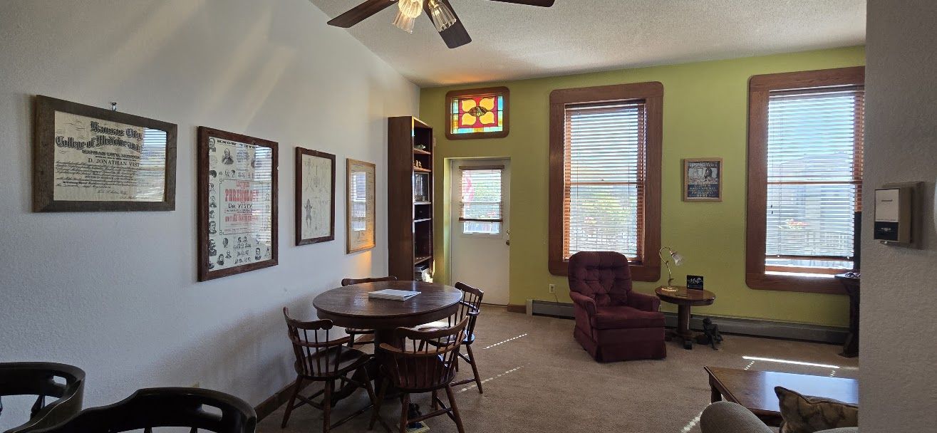 A room with a dining table, chairs, a red armchair, a bookshelf, and a window with blinds.