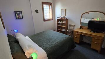 A bedroom with a bed, a desk with a computer, a chair, a bookshelf, and a window with blinds.