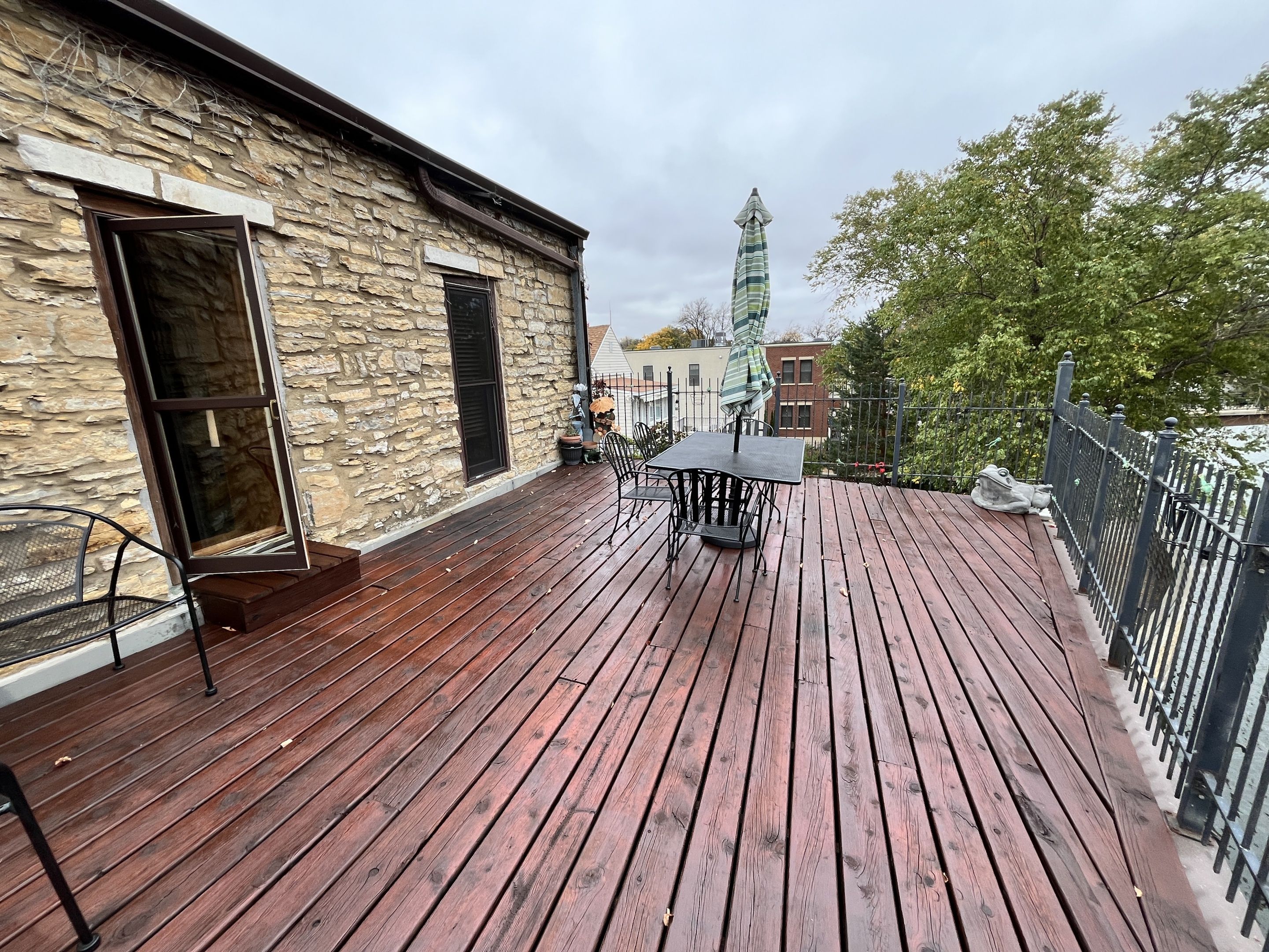 Eine Holzterrasse mit einem Steinhaus, einem Tisch mit Stühlen und einem Turm im Hintergrund.