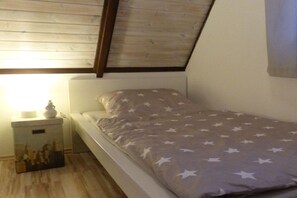 Un lit simple avec une couvre-lit à motifs étoilés, dans une pièce dotée d’un plancher en bois et d’un plafond en pente.