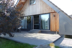 A modern house with a wooden exterior, large glass windows, and a patio area. - Holiday home with 3 bedrooms (Wurster Nordseeküste, Dorum- Neufeld)