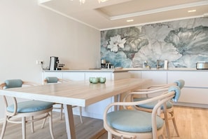 A dining area with a wooden table and chairs, a kitchen with a floral mural, and a coffee machine. - Holiday apartment with 2 bedrooms (Timmendorfer Strand)
