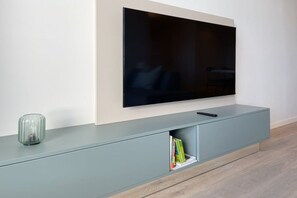 Een flatscreen televisie bevestigd aan een muur boven een grijze entertainmentkast met een glazen vaas en boeken.