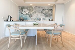 Een eetgedeelte met een witte tafel, zes stoelen en een bloemenmural op de muur.