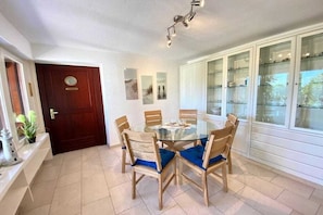 A dining area with a round glass table surrounded by wooden chairs with blue cushions, a dark wooden door, and white cabinets with glass doors. - Holiday home with 3 bedrooms (Sierksdorf)