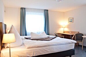 A hotel room with a bed, bedside lamp, desk, chair, and a window with curtains. - Holiday home Baltic Sea barrier-free (Waabs)