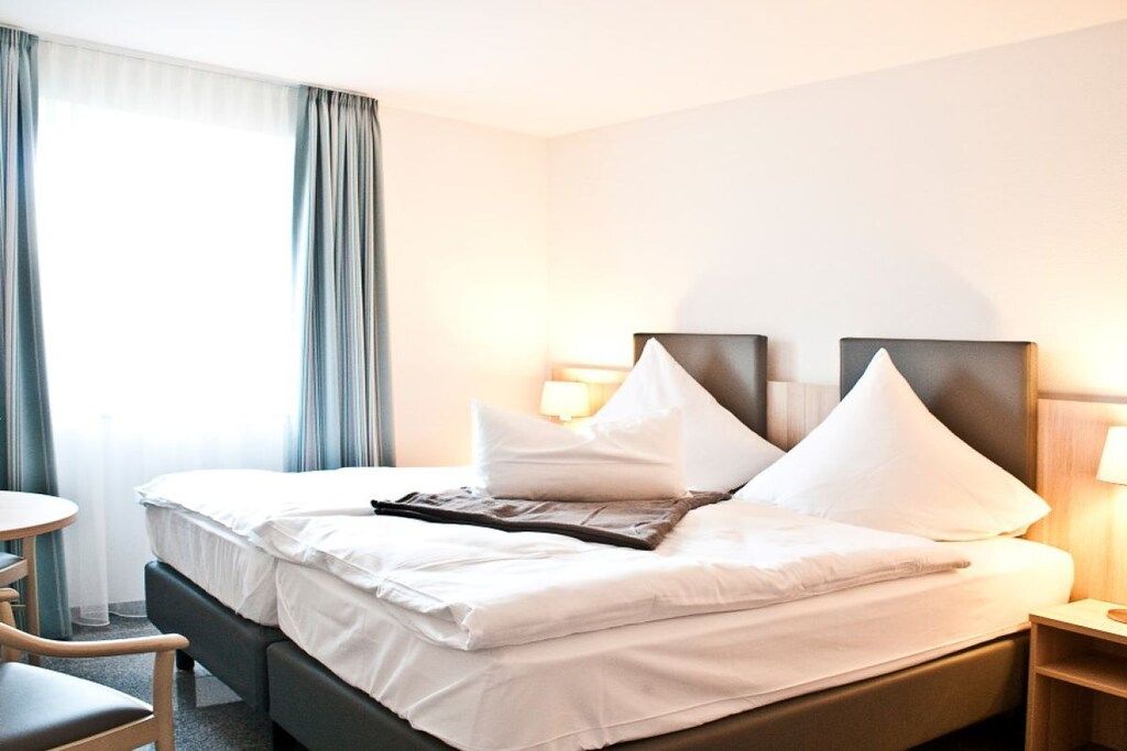 A hotel room with a bed, bedside tables, a chair, and curtains.