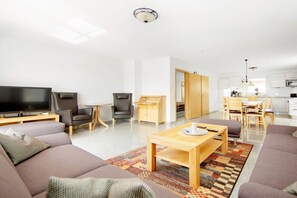 A modern living room with a flat-screen TV, sofas, a coffee table, and a dining area with chairs and a table. - Holiday home Baltic Sea barrier-free (Waabs)