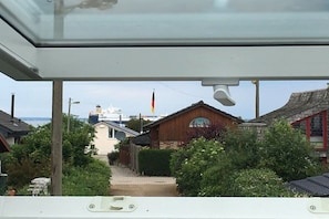A view from a window overlooking a residential area with a house, a flag, and a distant ship. - Strandhus (formerly Sternenhimmel) (Lübeck)