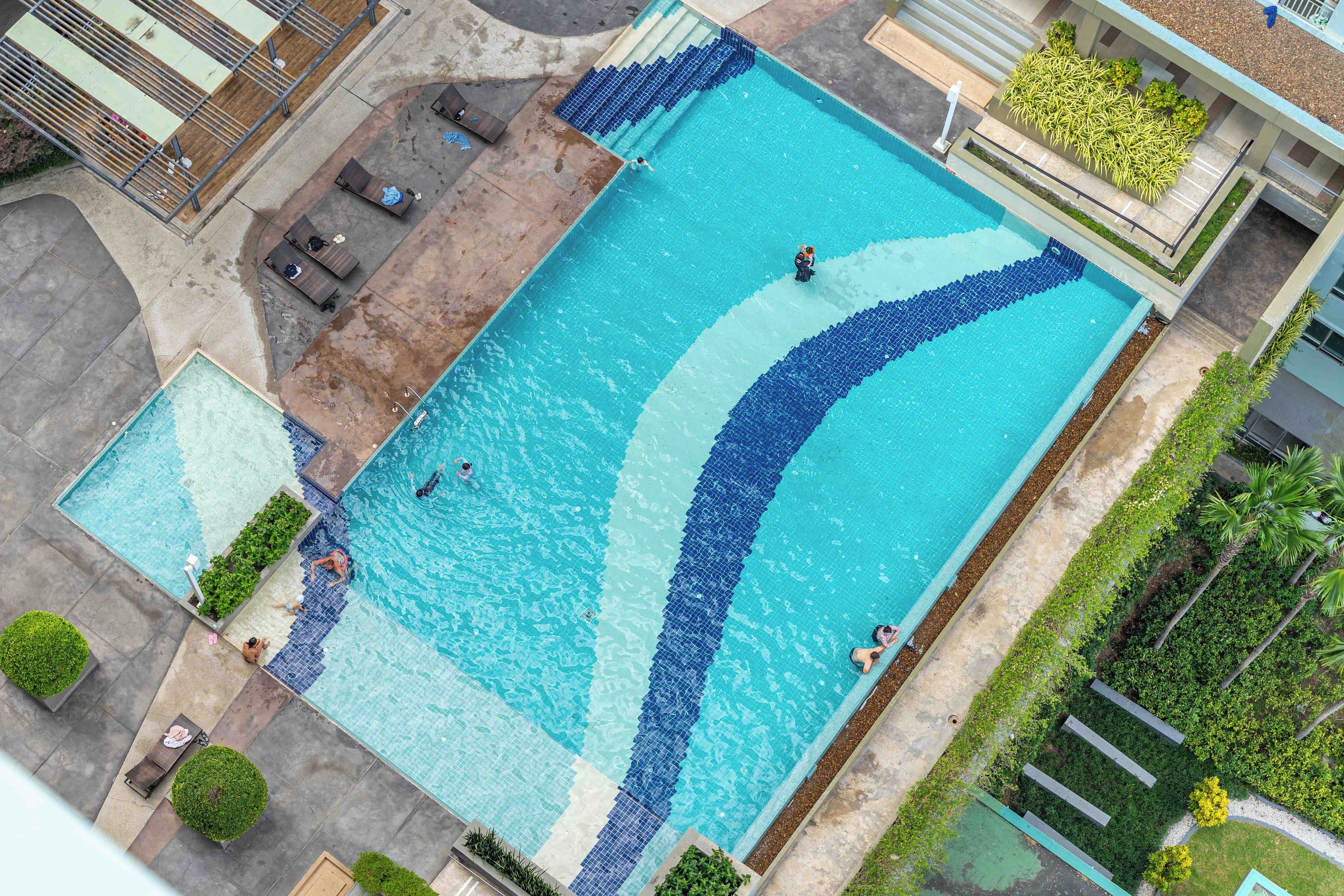 En stor rektangulär swimmingpool med en kant av kakel, omgiven av en betongplattform och några solstolar.