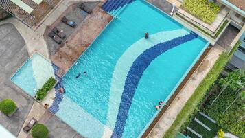 En stor rektangulär swimmingpool med en kant av kakel, omgiven av en betongplattform och några solstolar.