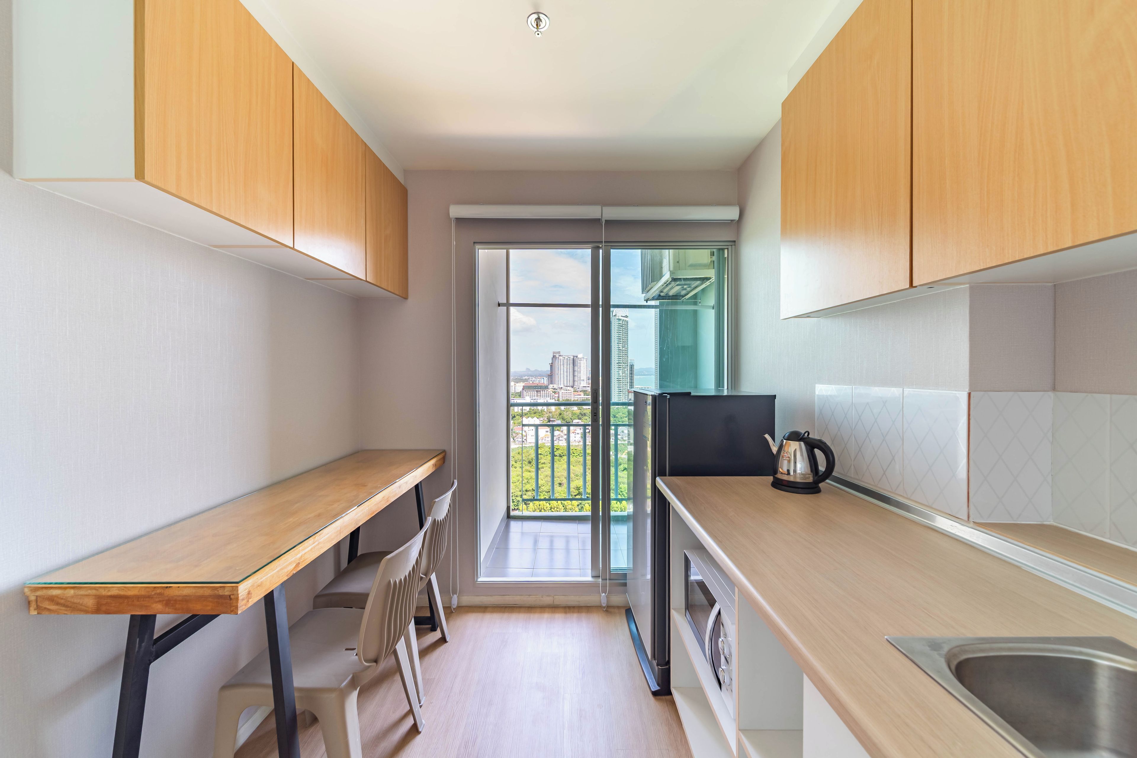 Una cocina moderna con armarios de madera, un lavamanos de acero inoxidable y vistas a un paisaje urbano a través de una puerta de vidrio.
