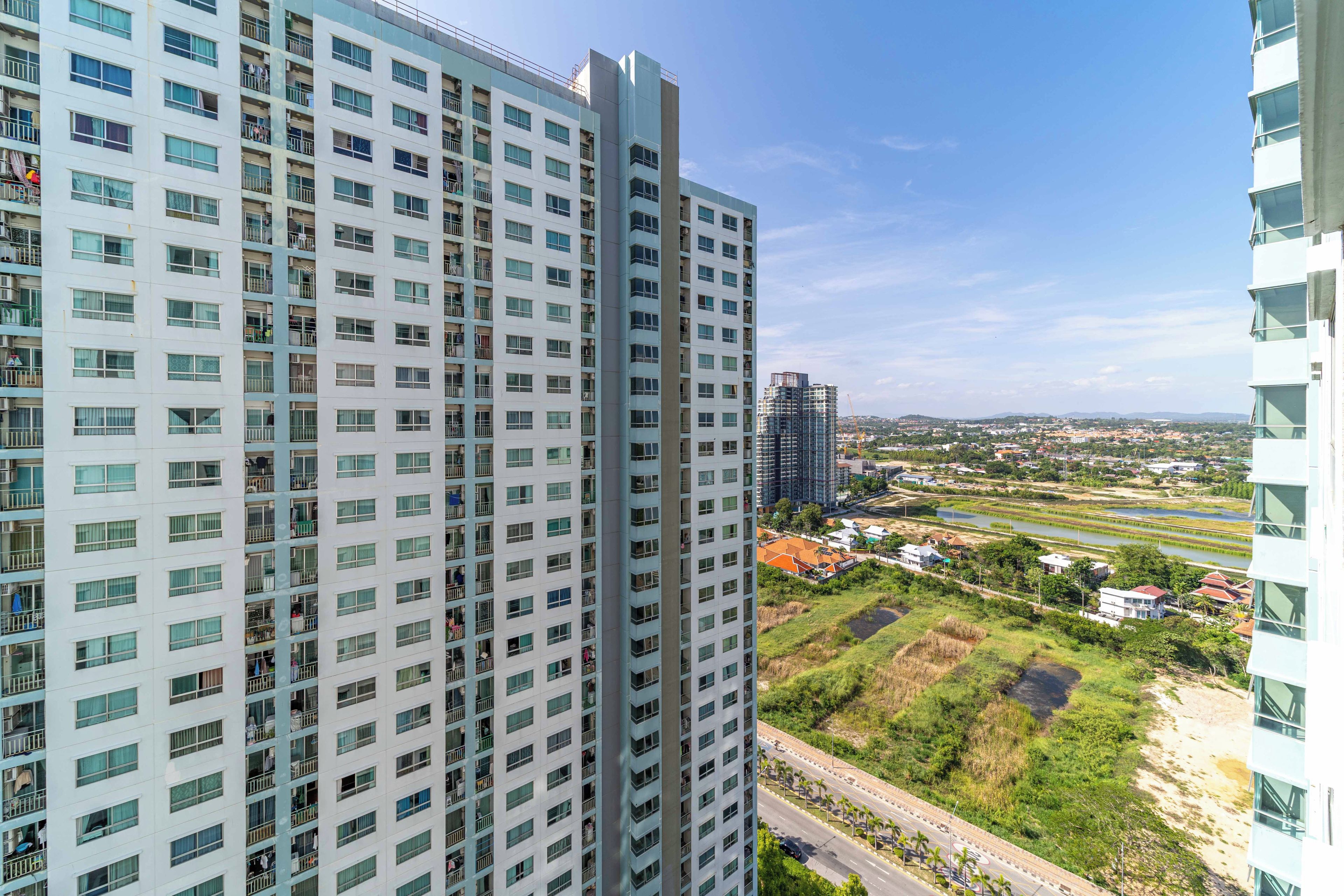 Un edificio alto con varios pisos y balcones, con vistas a un río y un área verde con árboles.