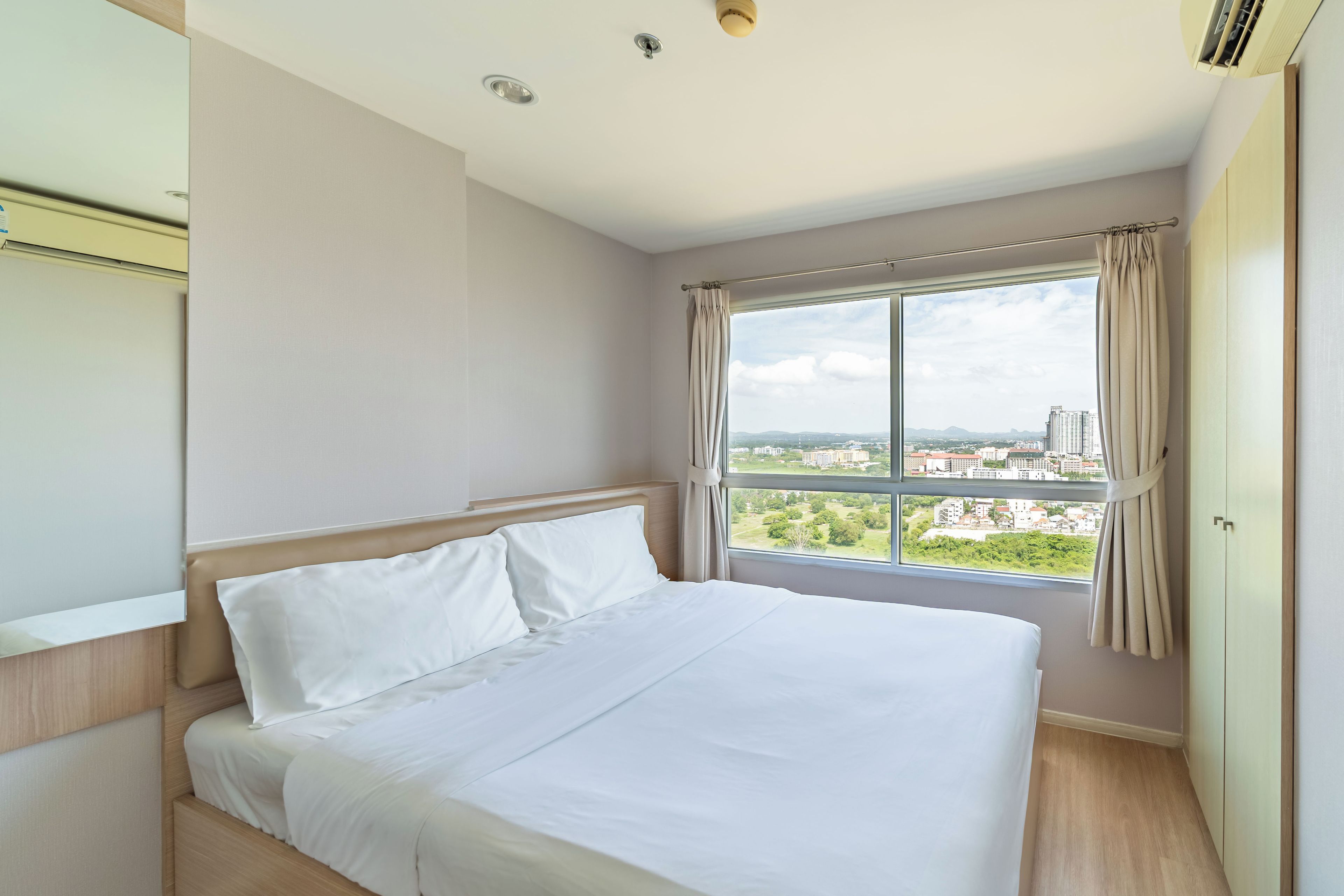 Habitación de hotel con una cama grande, una ventana con cortinas y vistas a la ciudad.