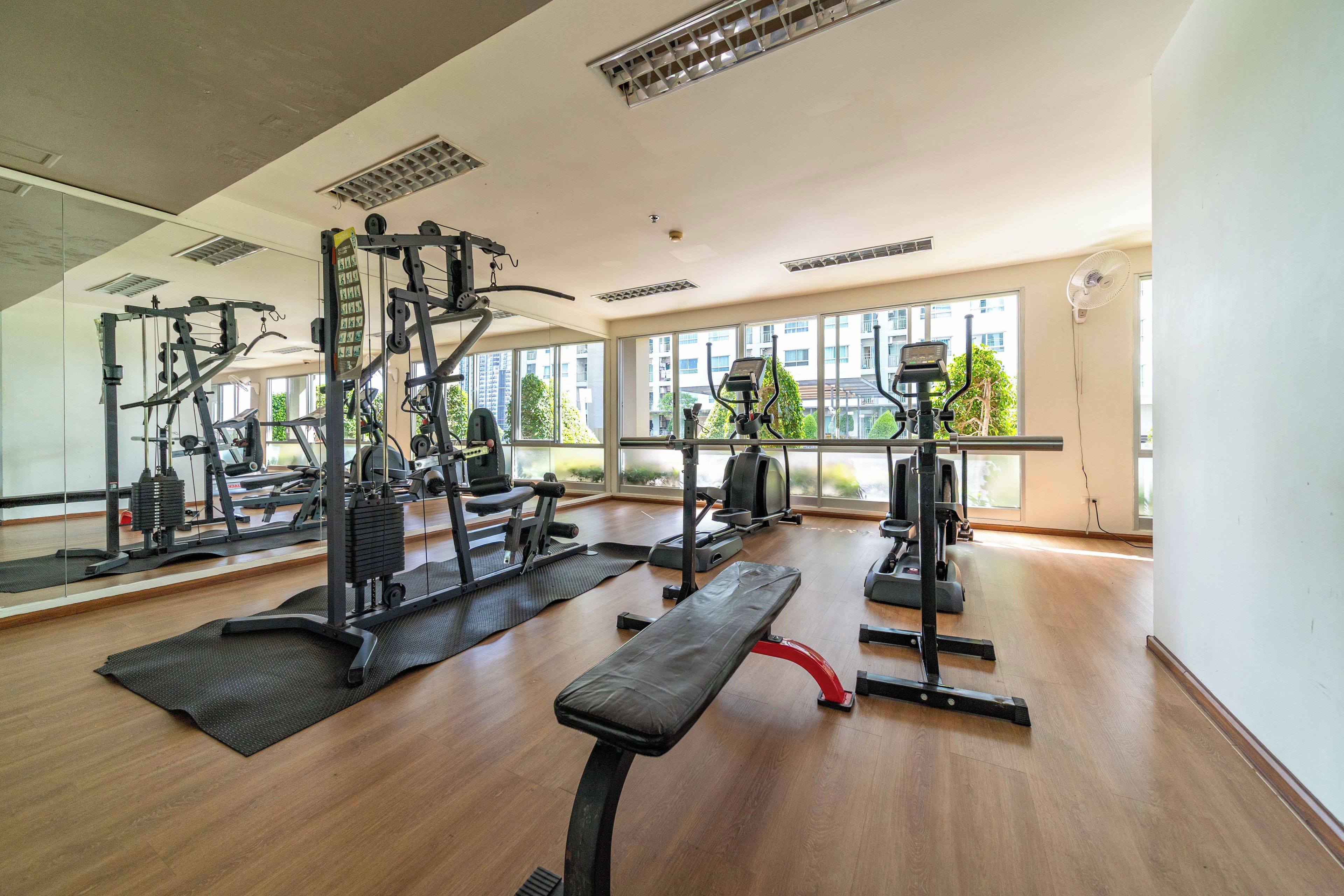 Ein Fitnessstudio mit unterschiedlichen Trainingsgeräten, großen Fenstern und einem Holzboden.