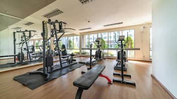 A gym with various exercise equipment, large windows, and a wooden floor.