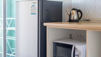 A kitchen with a refrigerator, microwave, kettle, and wooden cabinets.