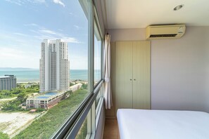 Una habitación de hotel con un ventanal grande, una cama, un armario y un equipo de aire acondicionado.