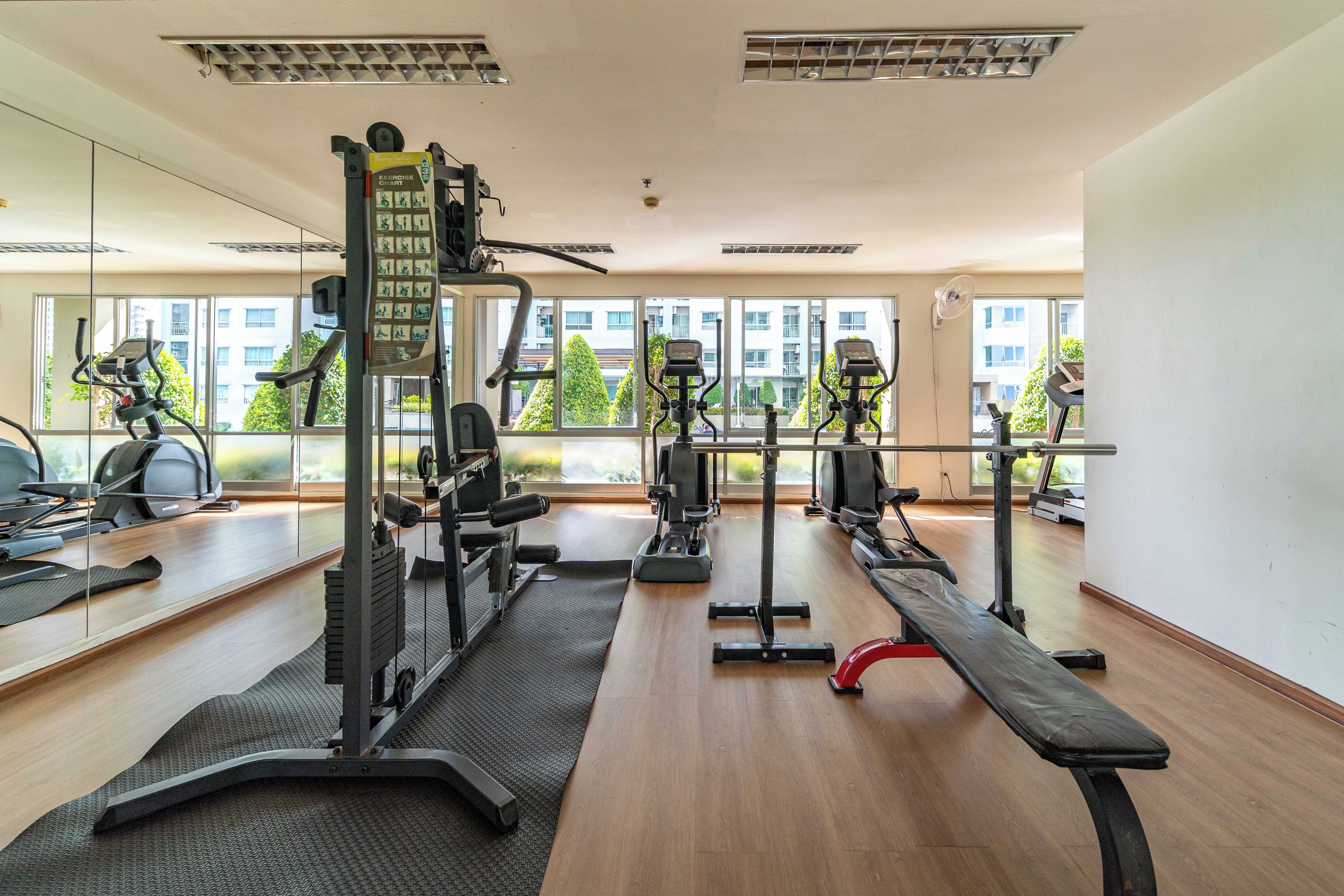 Ett gym med olika typer av träningsutrustning, stora fönster och utsikt över byggnader utanför.