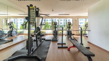 Ett gym med olika typer av träningsutrustning, stora fönster och utsikt över byggnader utanför.