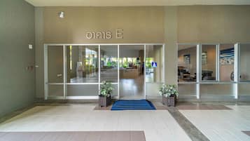 A hotel entrance with a tiled floor, a blue carpet, and potted plants.