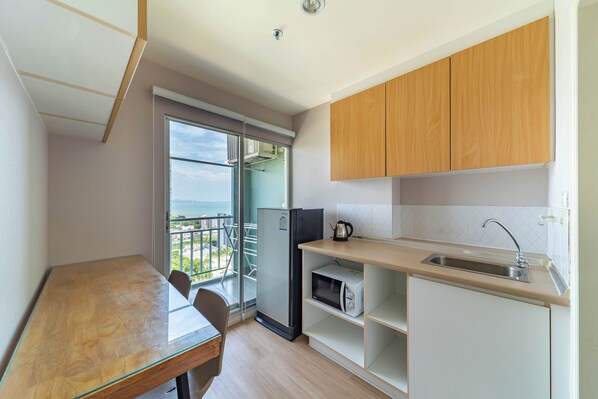 A compact kitchen with a dining area, a refrigerator, a microwave, and a view of the sea through a sliding door. - Sea View 22 at Lumpini Jomtien (Pattaya)
