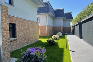 A residential building with a brick facade, a paved pathway, and a small garden area with flowers. - Holiday apartment in Damp with swimming pool (Damp)