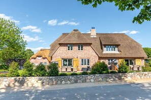 A large brick house with a thatched roof, multiple windows, and a stone wall in front.