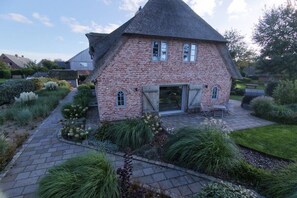 A brick house with a steeply pitched roof, a paved patio, and a garden with various plants.
