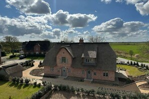 A large brick house with a thatched roof, surrounded by a well-maintained garden and a clear sky.