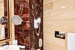 Casa de banho com parede de mármore, espelho, lavatório, secador de cabelo e telefone.