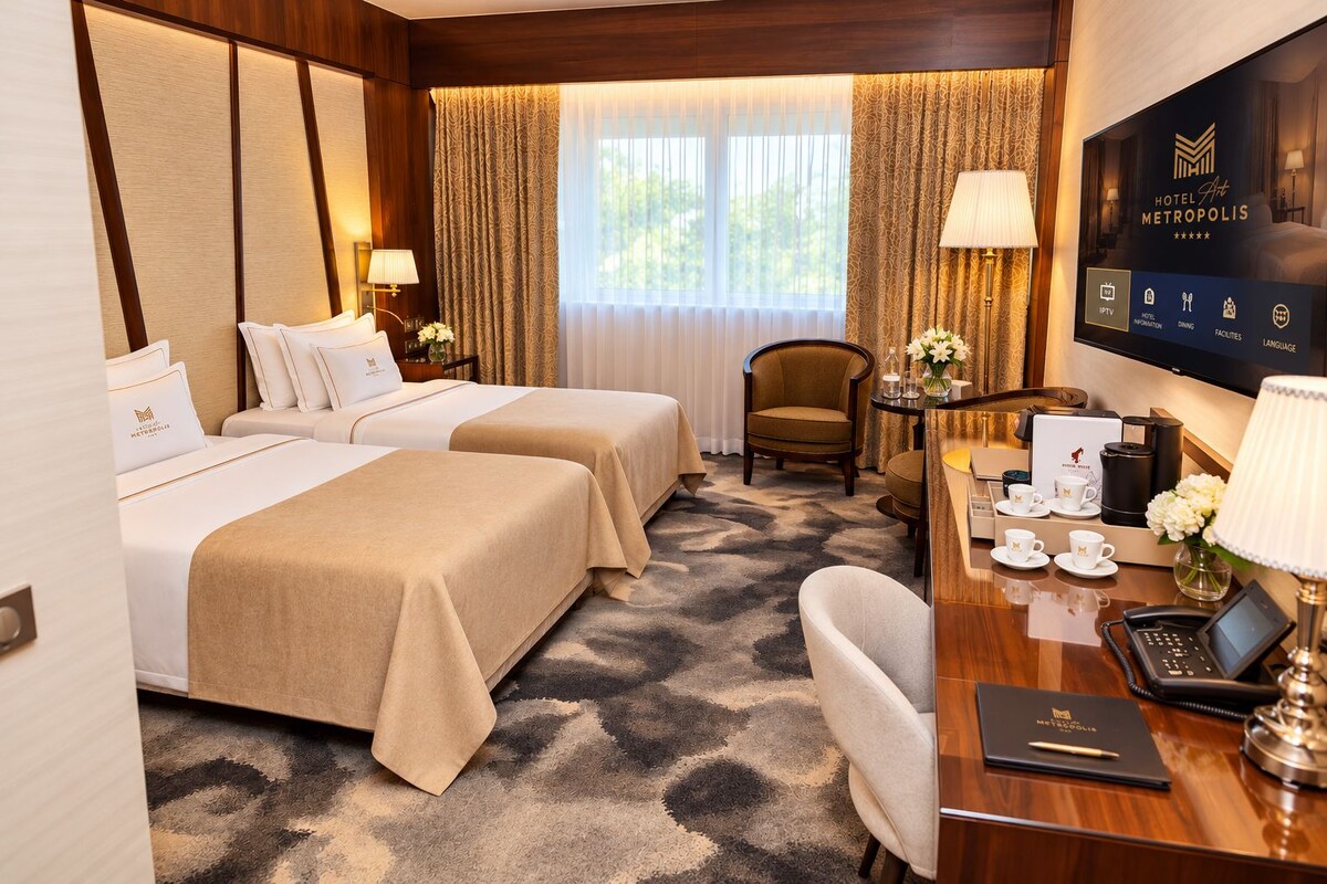 Quarto de hotel com duas camas, uma mesa de escritório com um laptop, uma cadeira, uma TV e uma máquina de café.