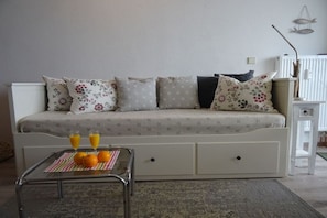Ein Schlafzimmer mit Schlafsofa, Nachttisch mit Lampe und kleinem Tisch mit Orangen und Saft.