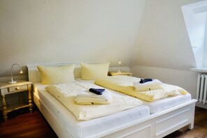 Ein ordentlich bezogenes Bett mit Kissen und zusammengefalteten Decken, ein Nachttisch mit Lampe und ein Heizkörper an der Wand.