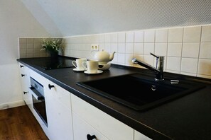 Eine Küche mit schwarzer Arbeitsplatte, weißen Schränken, einem schwarzen Spülbecken und einer weißen, gefliesten Spritzschutzwand.