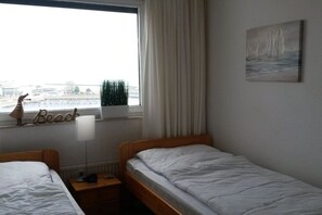 A bedroom with two single beds, a window with a view of buildings, a painting on the wall, and a lamp on the nightstand. - Holiday apartment in Damp with swimming pool (Damp)