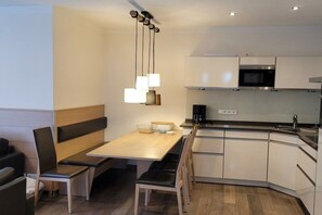 A modern kitchen with a wooden dining table, built-in cabinets, and a black microwave. - Villa Rossini - No. 4 (Norderney)