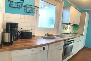 A kitchen with white cabinets, a Bosch dishwasher, a coffee maker, a kettle, a stove, and a window with a view. - ||----------------------Ahoy with garden---------------------|| (Dahme)