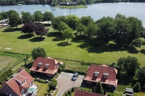 A residential area with two houses, a paved driveway, and a body of water in the background. - Lüttje Huck/ Seeblick 4 (Aurich)