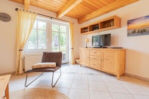 A living room with a wooden ceiling, a television, a cabinet, and a window with curtains. - Lüttje Huck/ Seeblick 4 (Aurich)