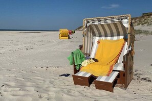 A beach chair with a striped canopy, a green towel, and a pair of sandals on the sand. - Holiday apartment with 1 bedroom (Norddorf)